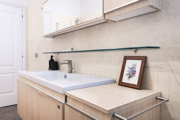 A bathroom with a white sink, a mirror, and a framed picture on the wall.
