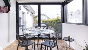 Un comedor moderno con una mesa de vidrio y sillas, una mesita auxiliar y vistas al exterior a través de amplias ventanas.