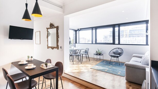 Una sala de estar moderna con comedor, ventanas grandes y vista a la ciudad.