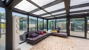 Una sala moderna con un sofá modular, un tapete estampado y ventanas amplias con vistas al exterior.