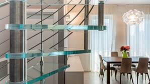 Un interior moderno con una escalera de cristal, un comedor con mesa y sillas, y una araña.
