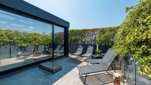 Un patio moderno al aire libre con paredes de vidrio, sillones de descanso y una planta en maceta.