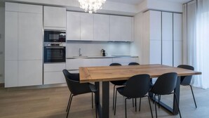 A modern kitchen with white cabinetry, a wooden dining table, and black chairs.