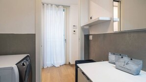 A modern hotel room with a washing machine, a small table with a mirror, and a door with a white curtain.
