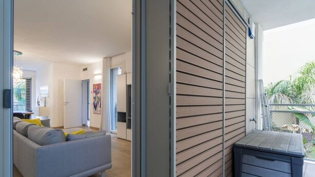A modern living room with a grey sofa, a wooden wall, and a small storage unit.