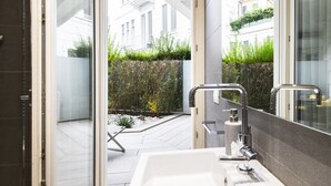 Een moderne badkamer met een ruime wastafel, een spiegel en uitzicht op een tuin en gebouwen.
