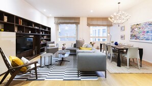 Een moderne woonkamer met een bank, fauteuil en salontafel, een eethoek met stoelen en een tafel, en een boekenplank.