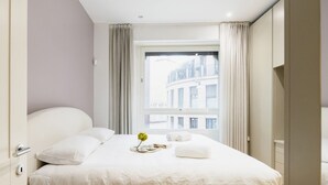Een moderne hotelkamer met een groot bed, een raam met gordijnen en uitzicht op gebouwen.
