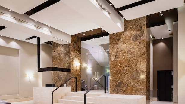 Een moderne hotel lobby met marmeren zuilen, een trap en een receptiebalie.