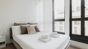 Une chambre d’hôtel moderne avec une grande fenêtre, un lit bien fait et une table de chevet avec une lampe.