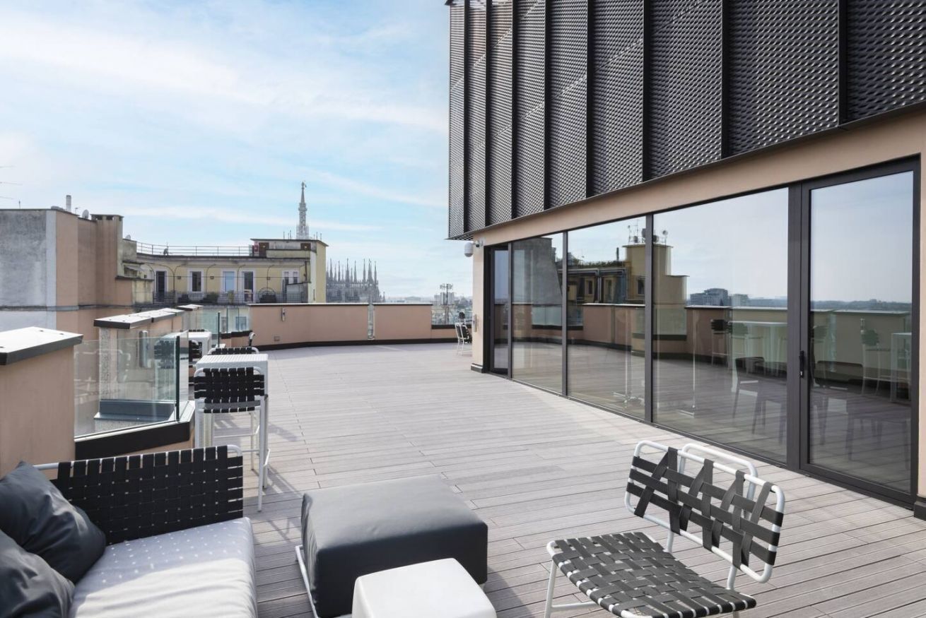 Eine Dachterrasse mit Sitzgelegenheiten im Freien, großen Fenstern und Blick auf die Stadtlandschaft.