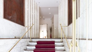 A marble staircase with red carpeted steps, flanked by white marble walls and wooden doors.