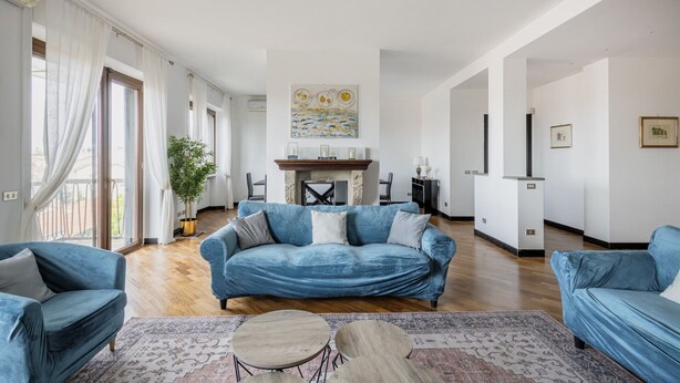 A spacious living room with a blue sofa set, a fireplace, and a large window with curtains.