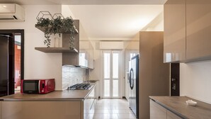 A modern kitchen with a built-in microwave, a gas stove, and a refrigerator. There is a window providing natural light and a plant on a shelf above the stove.