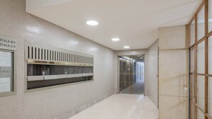 A hallway with a tiled floor, a wall-mounted shelf with items, and a door leading to another room.