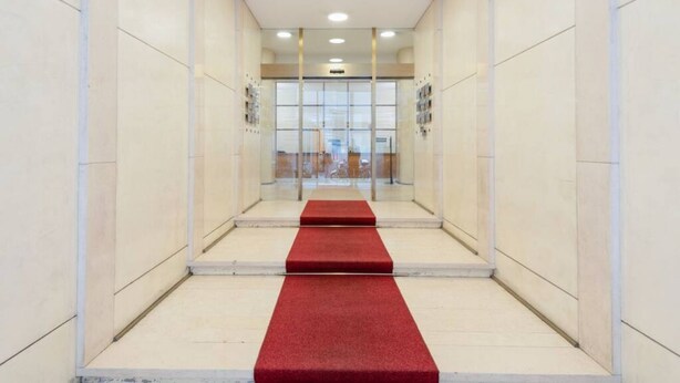 A hallway with a red carpet leading to a glass door entrance.