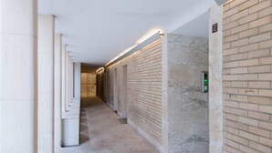 A corridor with a marble wall and a brick wall, leading to a door with a sign indicating a restroom.