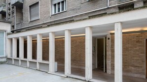 A building with a covered outdoor area supported by columns, featuring a brick facade and a door marked with a wheelchair symbol.