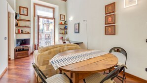A cozy living room with a wooden dining table, a sofa, and a TV. There are bookshelves and framed pictures on the walls. - Easylife - Refined apartment in Viale Montegrappa, 18 (Milano)