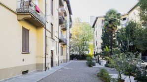 A narrow street with buildings on either side, featuring balconies with railings and potted plants.