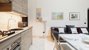 A modern kitchen with a sink, stove, and microwave, a dining area with a table set for two, and a living area with a sofa and a TV.