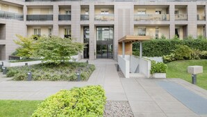 A multi-story residential building with balconies, a central entrance, and landscaped gardens.