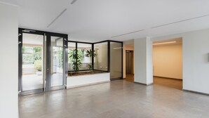 A spacious, modern interior with a glass partition, a small indoor garden, and a neutral color palette.