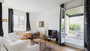 A modern living room with a white sofa, a dining table with chairs, a TV, and a large sliding glass door leading to an outdoor area. - Easylife - Charming house with terrace (Milano)