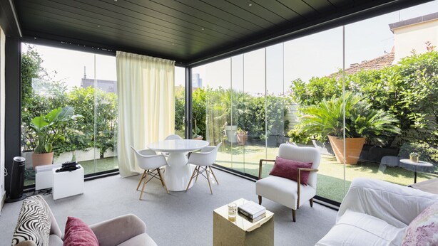 A modern living room with a glass wall, white furniture, and a variety of plants. - Easylife - Charming house with terrace (Milano)