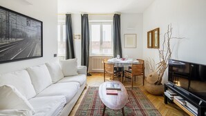 A living room with a white sofa, a round coffee table, a dining table with chairs, a television, and a large window with curtains. - Easylife - Charming house with terrace (Milano)