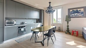 Una cocina moderna con armarios grises, una mesa de comedor con sillas, una araña y un ventanal con vistas.