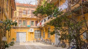 A narrow street with yellow buildings, bicycles parked along the sides, and a tree in the foreground. - Easylife - Brand, new and fully furnished apt (Milano)