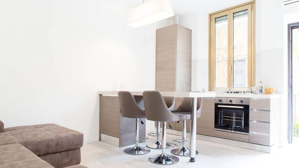 A modern kitchen with a built-in oven, a dining area with bar stools, and a large window with wooden shutters. - Easylife - Brand, new and fully furnished apt (Milano)