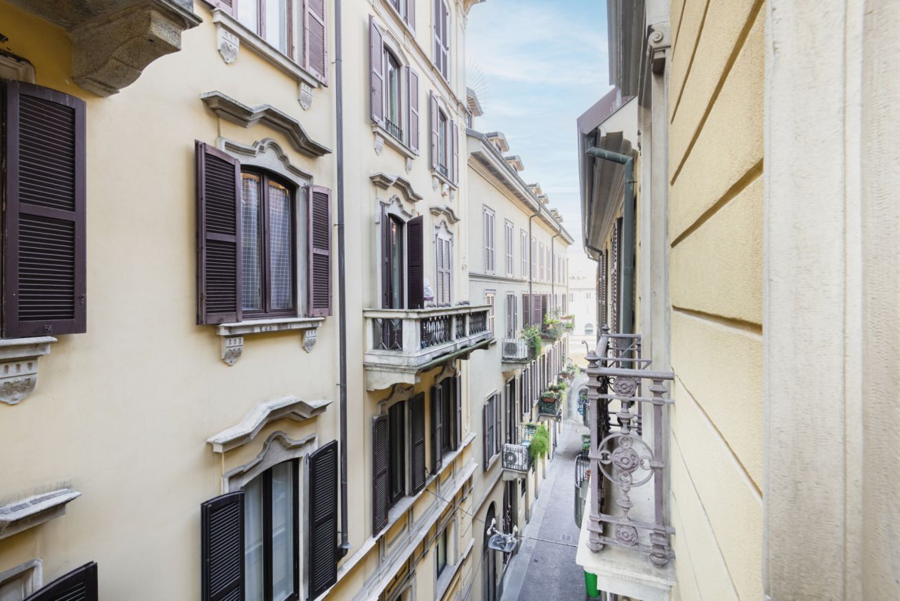 A narrow street with buildings featuring traditional architecture, balconies, and a clear sky.
