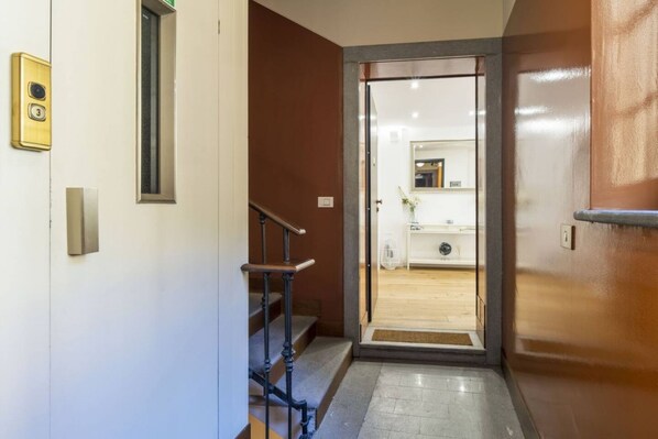 L’entrée d’un hôtel, avec un escalier en bois, une porte vitrée donnant sur un espace d’accueil et une petite plante d’intérieur.