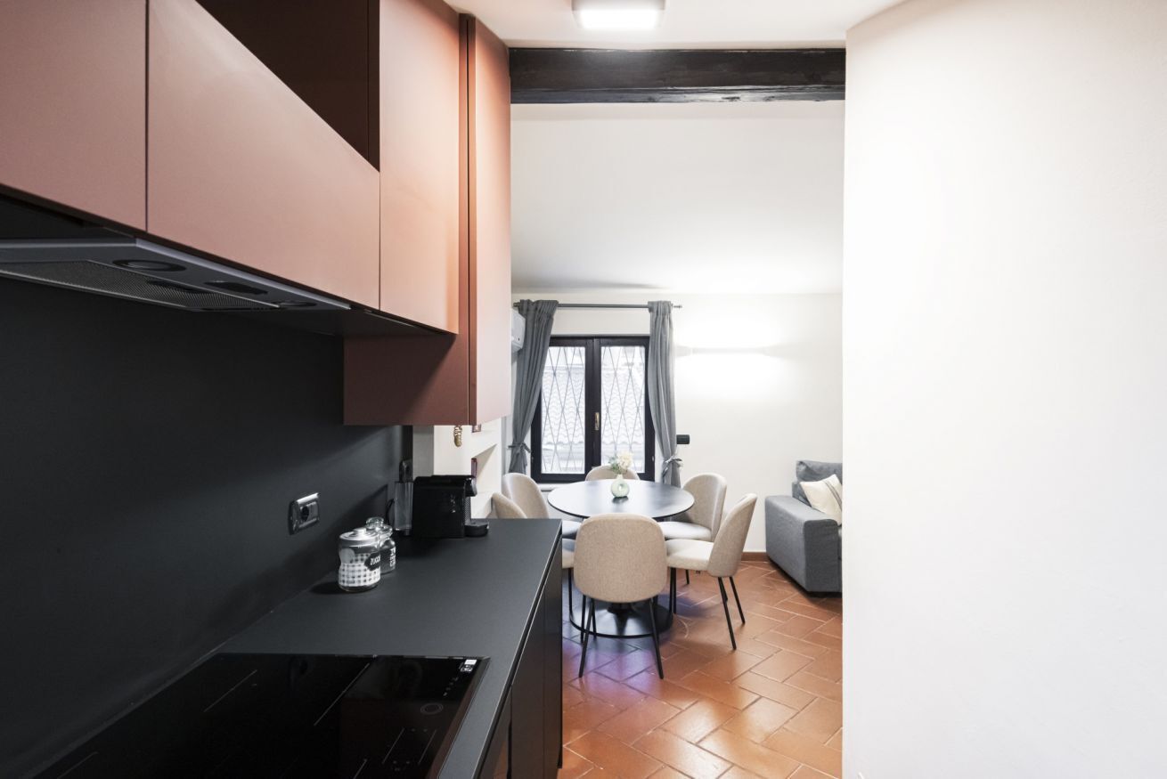 A modern kitchen with dark cabinetry, a black countertop, and a dining area with a round table and chairs.