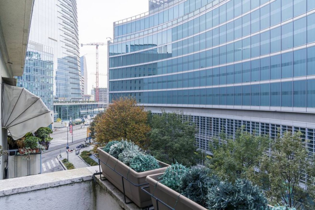 Un edificio moderno con facciata in vetro curvo, immerso nel verde e affiancato da una passeggiata pedonale.