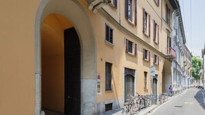 Une rue bordée d’un immeuble jaune, doté d’une entrée en arc de cercle, d’une rangée de fenêtres et de vélos garés à l’extérieur.