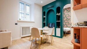 A modern kitchen with teal accent walls, white cabinetry, and a dining area with white chairs and a round table.