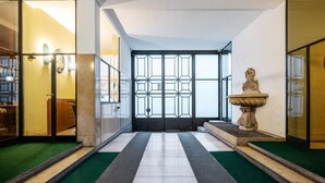A hallway with a geometric patterned glass door, a stone fountain, and a green carpeted floor.