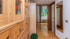 Un couloir avec des meubles de rangement en bois, une plante en pot et, au fond, une porte ouverte donnant sur une salle à manger.
