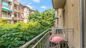 Un balcon orné d’une statue de flamant rose, entouré de verdure et de bâtiments résidentiels.