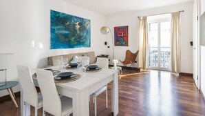 A dining area with a white table set for four, a large abstract painting on the wall, and a view of the outdoors through a glass door. - Easylife - Spacious apartment a few steps from Piazza Gae Aulenti (Milan)