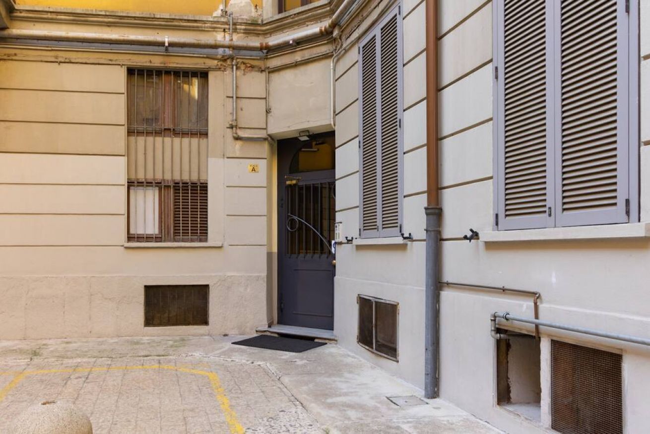 Une ruelle urbaine avec une entrée étroite, un portail en métal et une porte donnant accès à un immeuble.