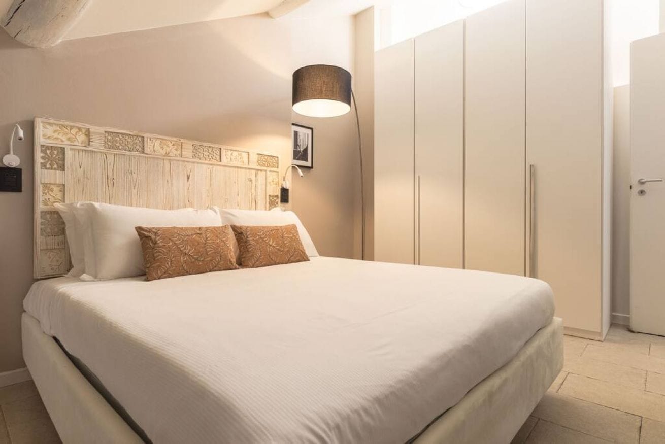 A bedroom with a large bed, a headboard with decorative panels, a bedside lamp, and a wardrobe.