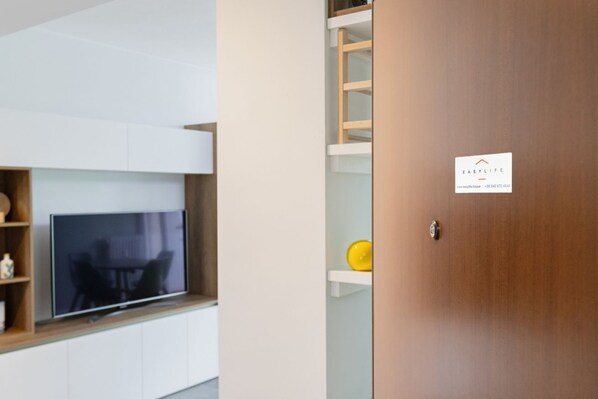 Un interior moderno con una puerta de madera, un televisor sobre un estante blanco y un objeto amarillo pequeño en otro estante.