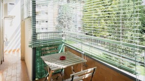 Un balcón con mesa y sillas, un tazón rojo y vistas a zonas verdes y edificios.