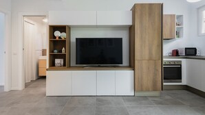 Una cocina moderna con televisor integrado, muebles blancos y una pared decorativa de madera.