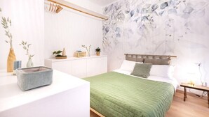 A bedroom with a bed, a bedside table, a nightstand, a wall with a floral pattern, and a hanging light fixture.