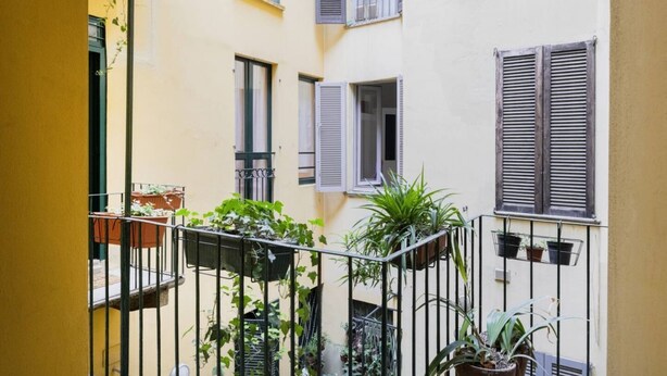 A yellow building with balconies, potted plants, and shutters.